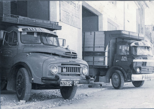Imagen en blanco y negro de dos camiones antiguos saliendo de una cochera