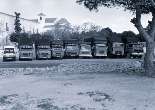 Imagen en blanco y negro de una fila de camiones vistos de frente delante de un santuario