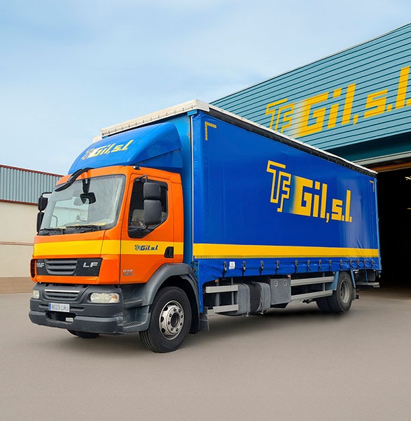 Camión de transporte de mercancías aparcado delante de una nave.