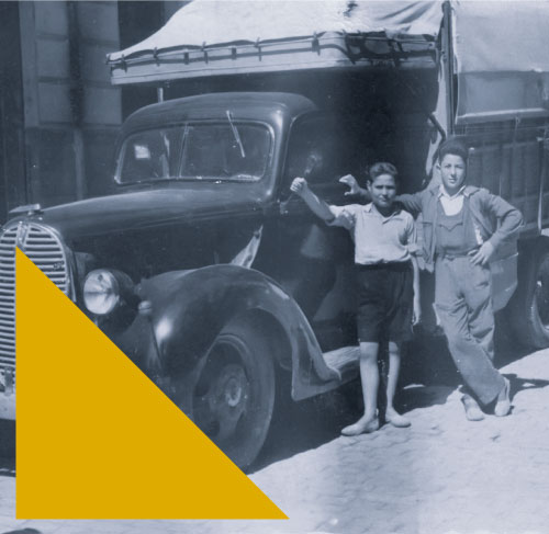 Foto antigua en blanco y negro en donde se ven dos chavales apoyados en un camión